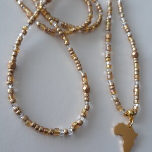 May include: A gold beaded necklace with a gold pendant shaped like the continent of Africa. The necklace is made of small gold and clear beads.