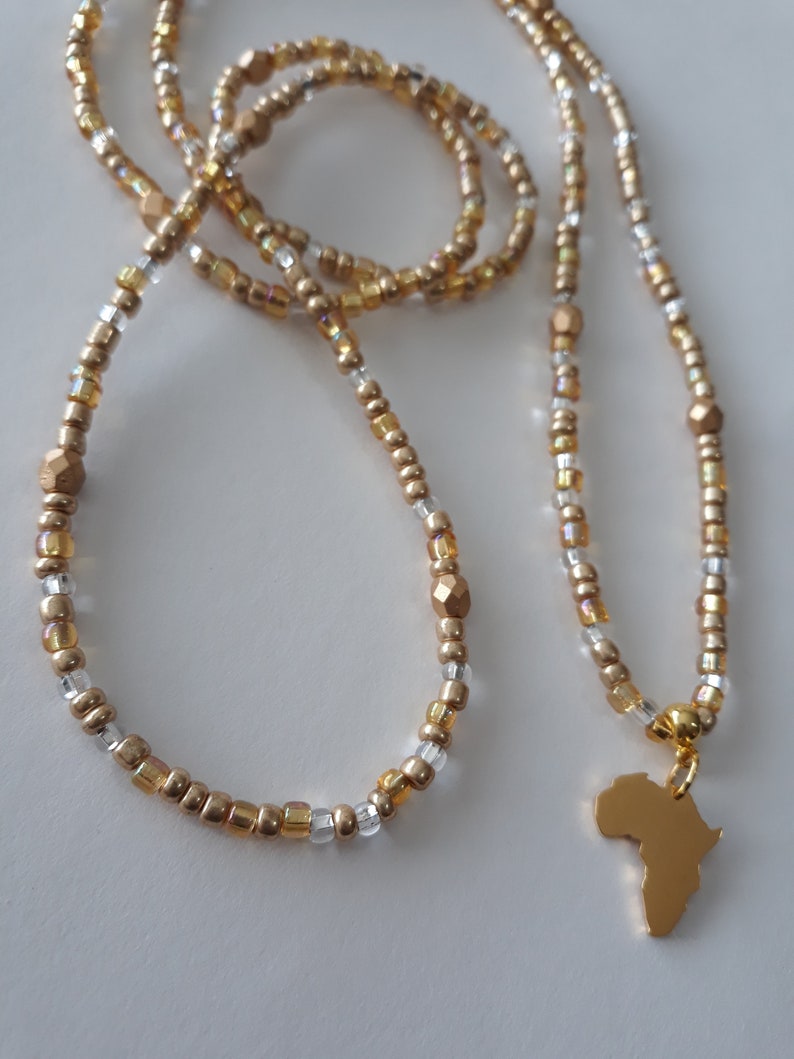 May include: A gold beaded necklace with a gold pendant shaped like the continent of Africa. The necklace is made of small gold and clear beads.
