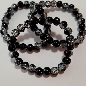 May include: Three black and silver beaded bracelets. The beads are round and have a speckled appearance.