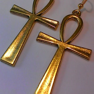 May include: A pair of gold-tone earrings featuring the Ankh symbol, an ancient Egyptian hieroglyph representing life.
