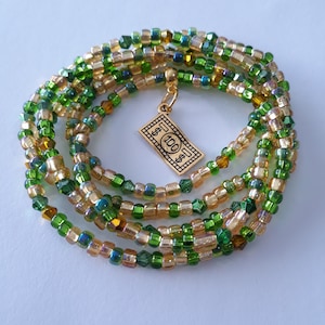 May include: A multi-strand waist bead necklace with green and gold beads. The necklace has a gold charm shaped like a dollar bill with the number "100" on it.