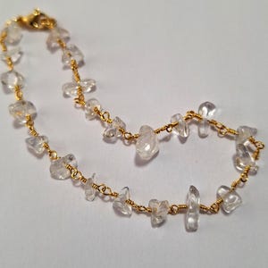 May include: A delicate gold chain bracelet with clear quartz stones. The stones are irregularly shaped and have a natural, raw look.