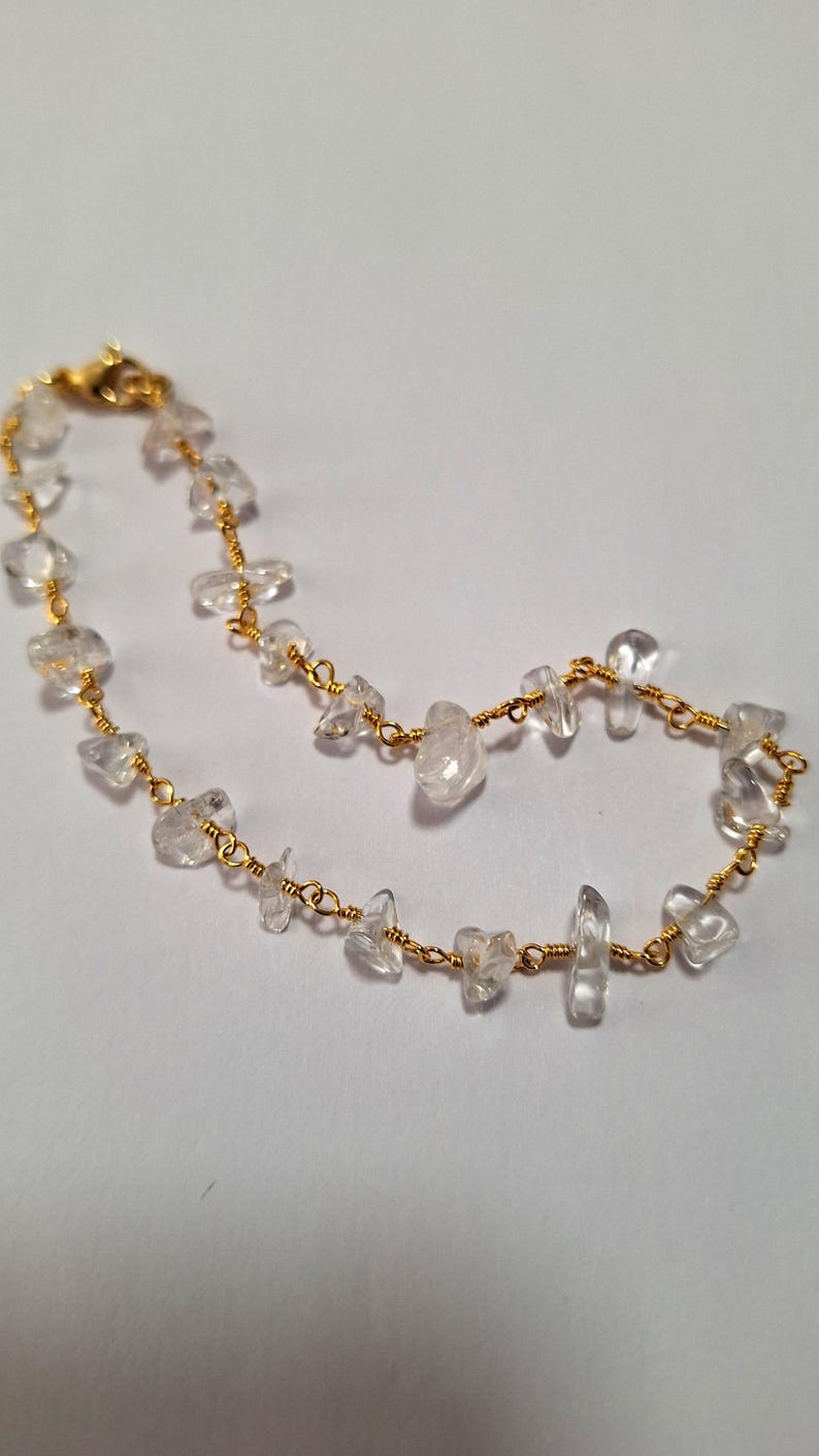 May include: A delicate gold chain bracelet with clear quartz stones. The stones are irregularly shaped and have a natural, raw look.
