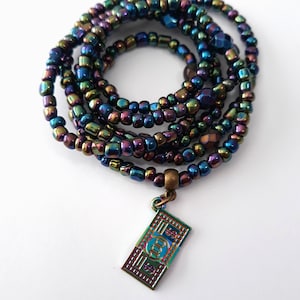 May include: A multi-strand beaded necklace with iridescent blue, green, and purple beads. The necklace has a charm in the shape of a $100 bill.