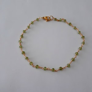May include: A delicate gold chain bracelet with small green gemstone beads.