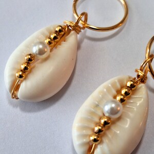 May include: A pair of white cowrie shell keyrings with gold wire wrapped around them and gold beads and white pearls strung along the wire.