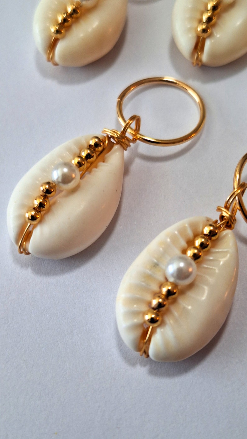 May include: A pair of white cowrie shell keyrings with gold wire wrapped around them and gold beads and white pearls strung along the wire.