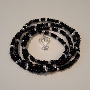 May include: A black beaded wrap bracelet with a silver charm in the shape of a heart with a swirl design.