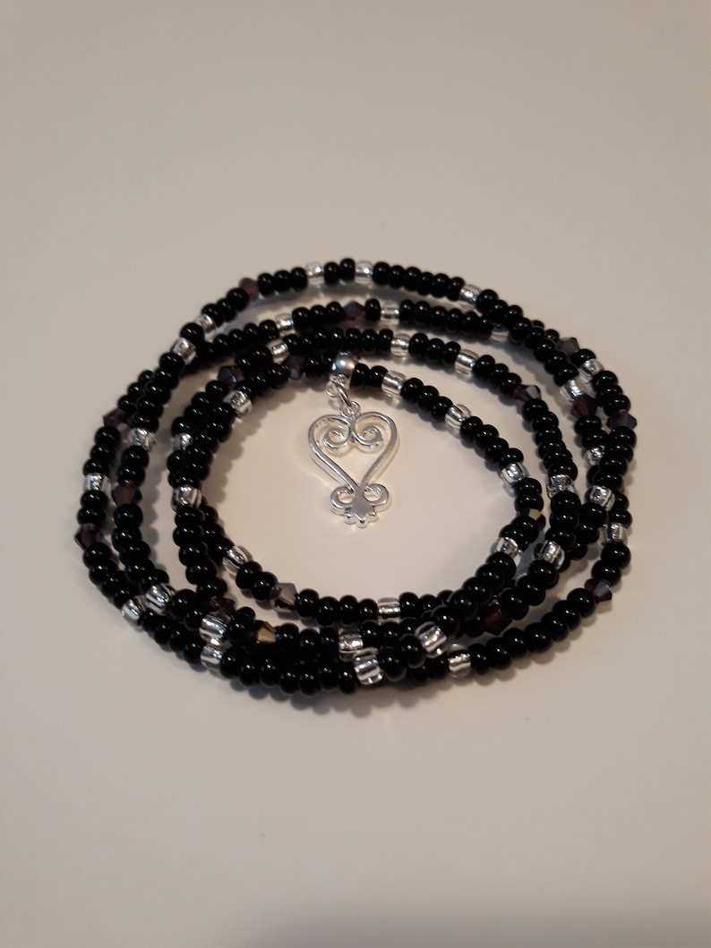 May include: A black beaded wrap bracelet with a silver charm in the shape of a heart with a swirl design.