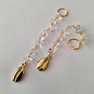 May include: A pair of gold earrings with clear crystal beads and a gold seashell charm on each earring.