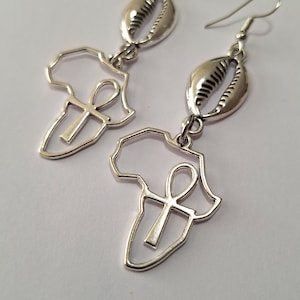 May include: Silver earrings featuring a cutout of the continent of Africa with an Ankh symbol inside, and a cowrie shell charm.