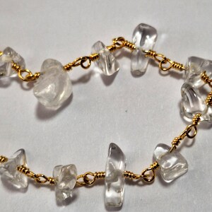 May include: A delicate bracelet made with clear quartz stones and gold wire. The stones are irregularly shaped and have a natural, raw look. The gold wire is thin and wraps around each stone, creating a simple and elegant design.