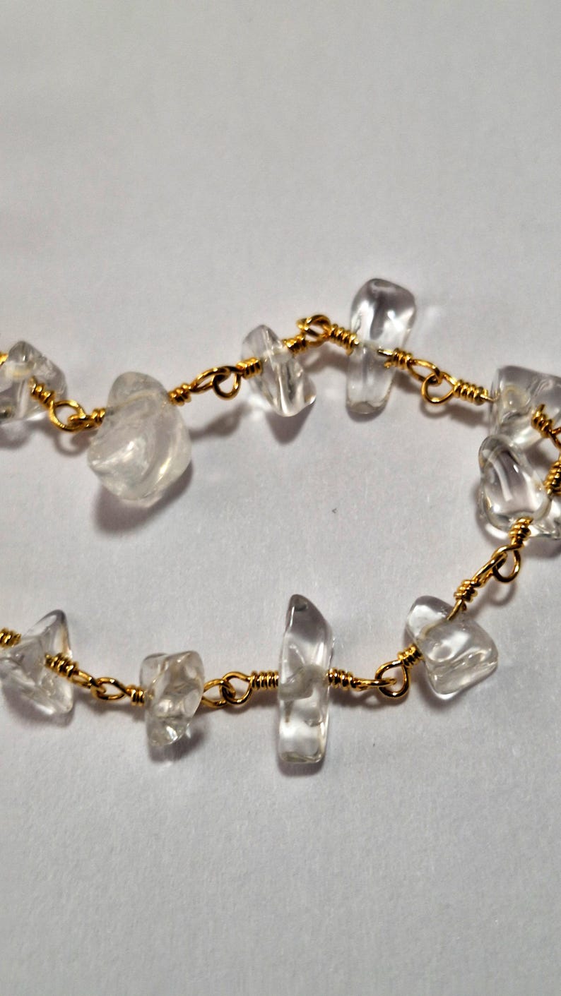 May include: A delicate bracelet made with clear quartz stones and gold wire. The stones are irregularly shaped and have a natural, raw look. The gold wire is thin and wraps around each stone, creating a simple and elegant design.