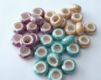 May include: A collection of ceramic beads in three colors: teal, beige, and purple. The beads are iridescent and have a glossy finish.
