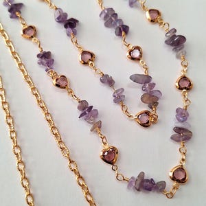 May include: Gold-colored chain necklaces with purple amethyst chips and pink heart-shaped accents. The necklaces are displayed on a white background, showcasing the jewelry's delicate design and color contrast.
