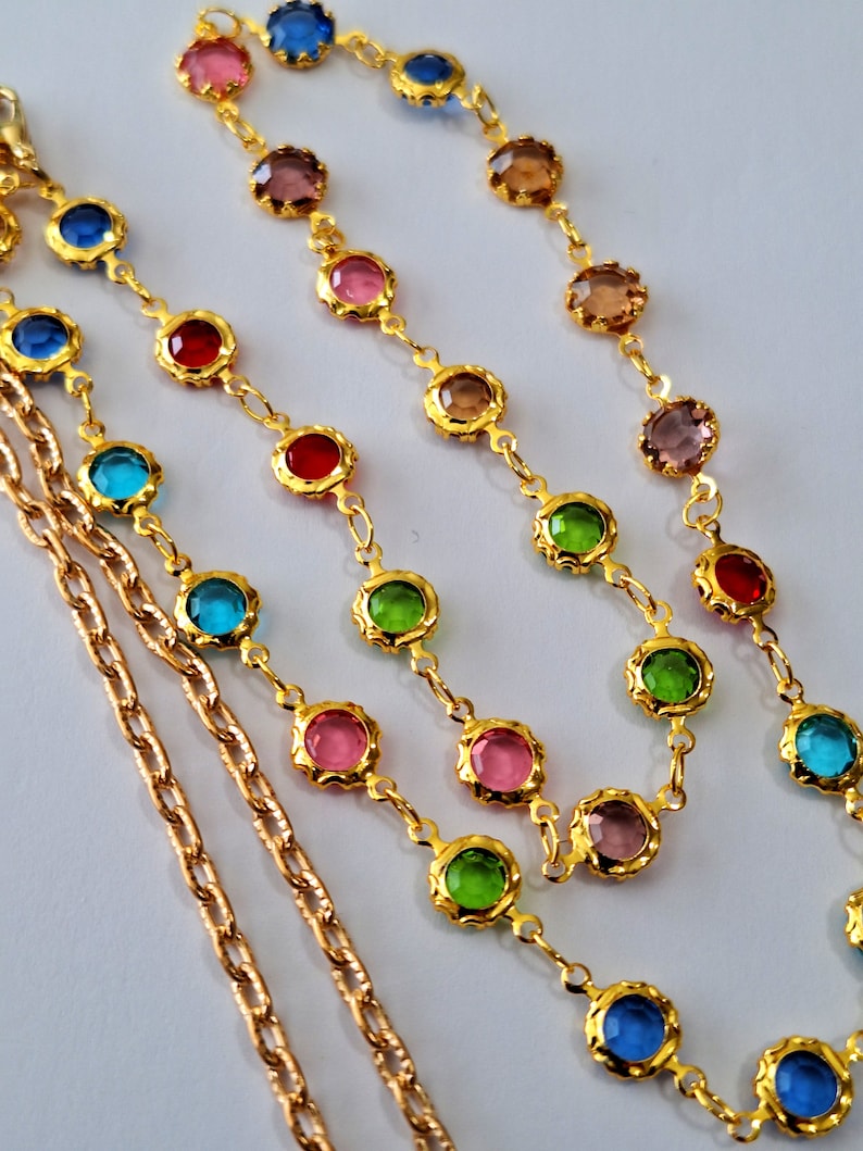 May include: Two gold chains with colorful round glass beads. The beads are in shades of pink, blue, green, and red.