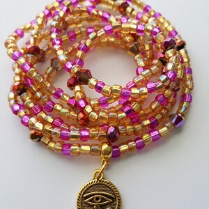 Puede incluir: Una cadena de cintura con cuentas en tonos dorados, rosas y burdeos. Las cuentas est&aacute;n ensartadas, formando m&uacute;ltiples hebras. Un colgante dorado con un dise&ntilde;o de Ojo de Horus cuelga de la cadena. Un accesorio decorativo.