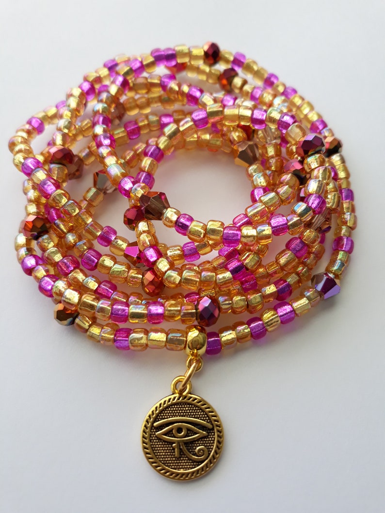 Puede incluir: Una cadena de cintura con cuentas en tonos dorados, rosas y burdeos. Las cuentas est&aacute;n ensartadas, formando m&uacute;ltiples hebras. Un colgante dorado con un dise&ntilde;o de Ojo de Horus cuelga de la cadena. Un accesorio decorativo.