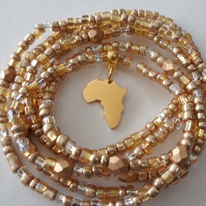 May include: Gold waist beads with a gold-colored Africa continent charm. The beads are made of small, round beads in a variety of sizes and shapes.