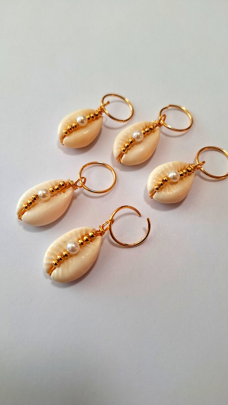 May include: Four gold hair clips with white seashells and pearl accents. Each clip has a gold ring attached to the top.