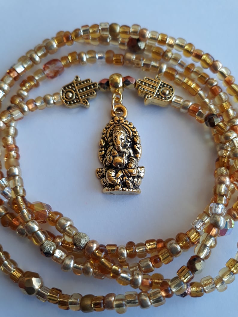May include: Gold beaded necklace with a gold Ganesha pendant and two gold hamsa charms.