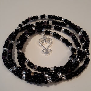 May include: A black beaded wrap bracelet with silver beads and a silver charm in the shape of an Adinkra symbol.