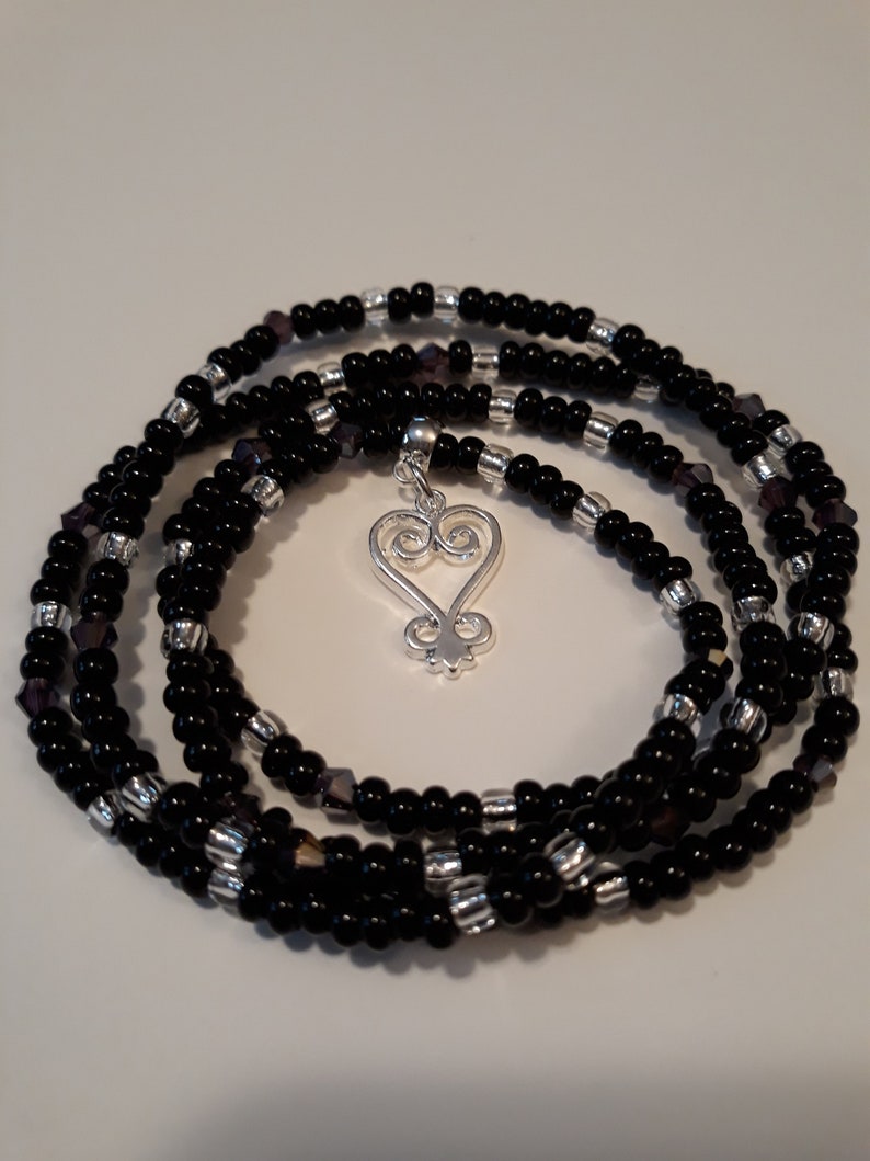May include: A black beaded wrap bracelet with silver beads and a silver charm in the shape of an Adinkra symbol.
