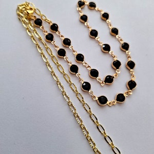 Puede incluir: Un collar de cadena de oro con un colgante de piedra preciosa negra. El collar est&aacute; superpuesto con una cadena de oro delicada.