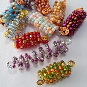 May include: A collection of colorful beaded hair wraps, each with a different color scheme and a wire coil at the end. The wraps are made of small, iridescent beads and are arranged in a circular pattern.
