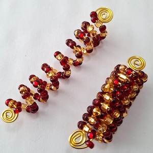 May include: Three beaded hair accessories. Two are spiral-shaped, and one is cylindrical. The beads are a mix of red and gold, with gold wire accents. The accessories are on a white background.
