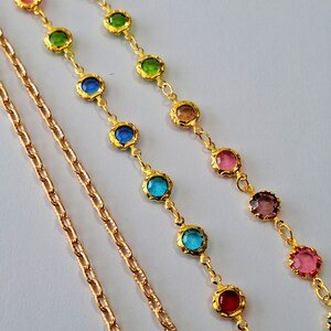 May include: Three gold chains with colorful round gemstones. The chains are layered on a white background.