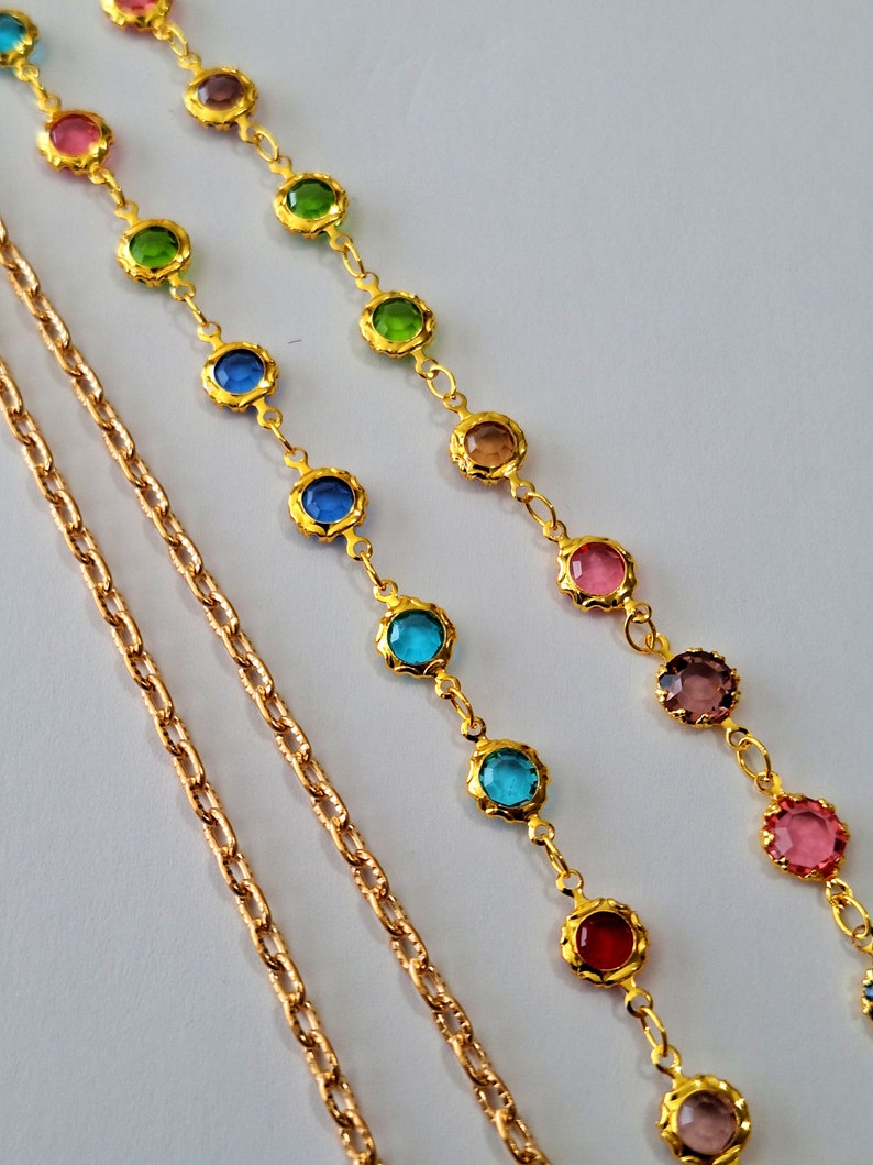 May include: Three gold chains with colorful round gemstones. The chains are layered on a white background.