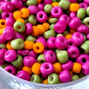 May include: A bowl filled with colorful beads in shades of green, pink, and orange. The beads are small and round, and they are arranged in a random pattern.