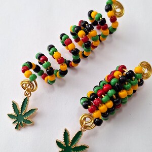 May include: Three hair accessories with a spiral design. The accessories are made of colorful beads in red, yellow, green, and black. Each accessory has a gold-colored wire base and a green leaf charm.