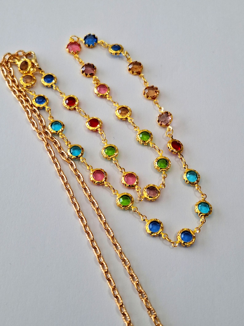 May include: A gold chain necklace with colorful round glass beads. The necklace is layered with a second gold chain.