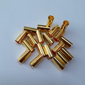 May include: A pile of gold-colored metal connector ends. The ends are cylindrical and have a smooth, shiny finish.