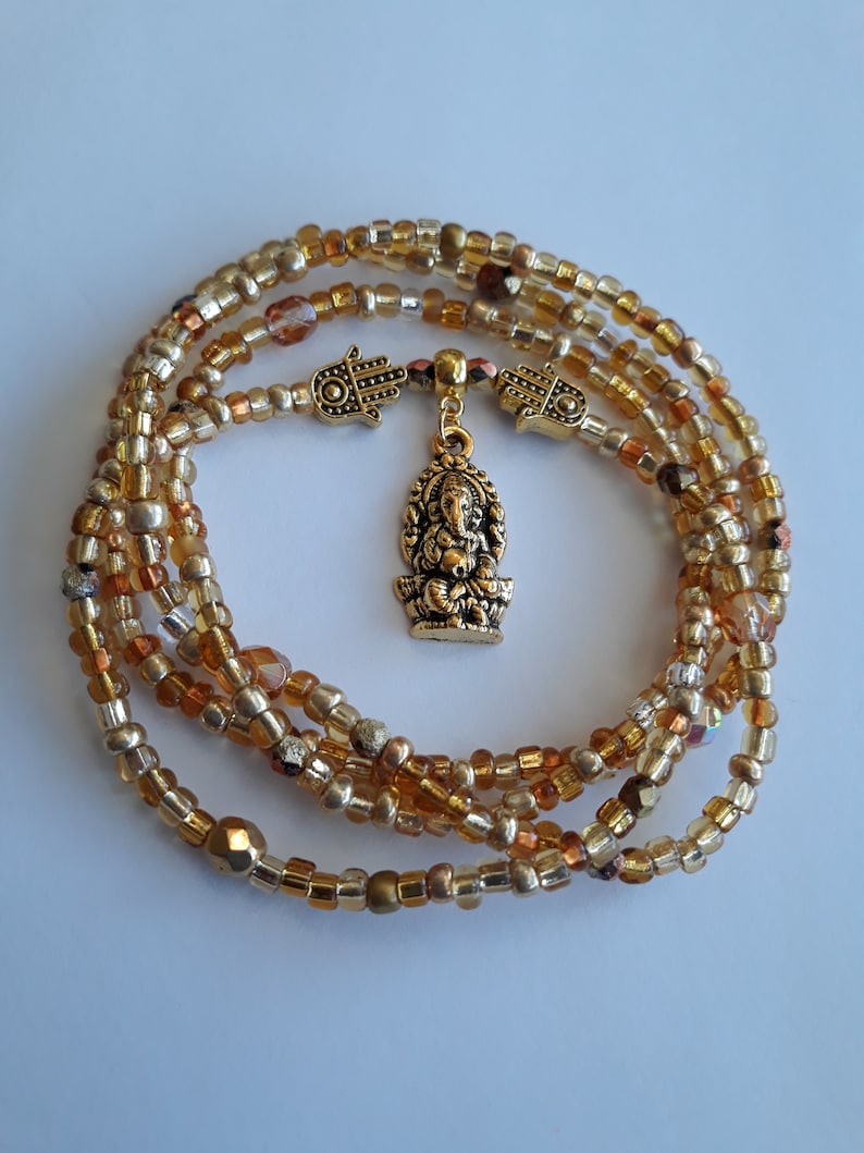 May include: A gold beaded waist chain with a gold Ganesha charm and two gold Hamsa charms.