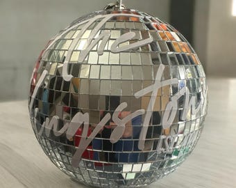 May include: A silver disco ball with the words "The Longest Story" written on it in white.