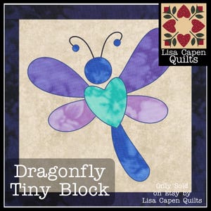 May include: A blue and purple dragonfly quilt block with a teal heart in the centre. The block is on a beige background with the text "Dragonfly Tiny Block" and "Only Sold on Etsy by Lisa Capen Quilts" below it.
