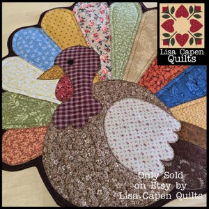 May include: A patchwork turkey-shaped quilt featuring a range of patterned fabrics in brown, red, blue, green, and yellow. The turkey has a plaid head and a floral body. The text "Lisa Capen Quilts" is visible.