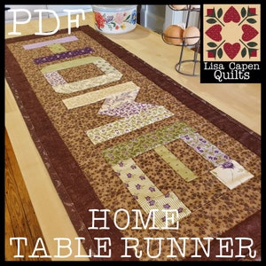 May include: A brown, green, and purple quilted table runner with the word "HOME" spelled out in large letters. The table runner has a brown border and is made of various floral patterned fabrics. The text "PDF" and "HOME TABLE RUNNER" is also visible in the image.