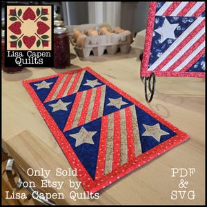 May include: A patriotic table runner with a red, white, and blue design featuring stars and stripes. The runner is rectangular and has a red border. The text "Only Sold on Etsy by Lisa Capen Quilts" is visible.