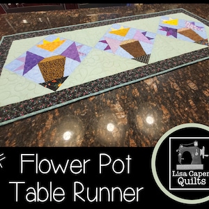 Pode incluir: Um padrão PDF para um corredor de mesa acolchoado com um design de vaso de flores. O corredor de mesa é feito com um fundo azul claro e apresenta três vasos de flores com tecido roxo, amarelo e marrom. O padrão é intitulado "Flower Pot Table Runner" e é de Lisa Capen Quilts.