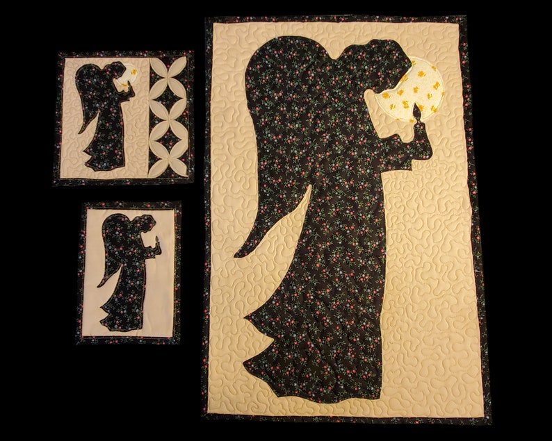 K&ouml;nnte beinhalten: Drei gequiltete Wandbeh&auml;nge mit der Silhouette eines Engels, der eine Kerze h&auml;lt. Der Engel ist schwarz mit einem Blumenmuster und der Hintergrund ist beige.