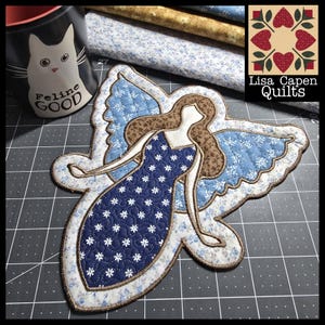 May include: A blue and white quilted angel applique with brown hair and a white outline. The angel is standing on a gray and black gridded surface. "Lisa Capen Quilts" is written in the upper right corner of the image.