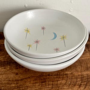 May include: Three white ceramic bowls with a crescent moon and yellow and pink stars design.