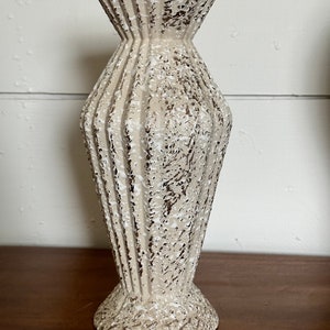 May include: A white ceramic vase with a textured, distressed finish. The vase has a wide mouth and a narrow base.