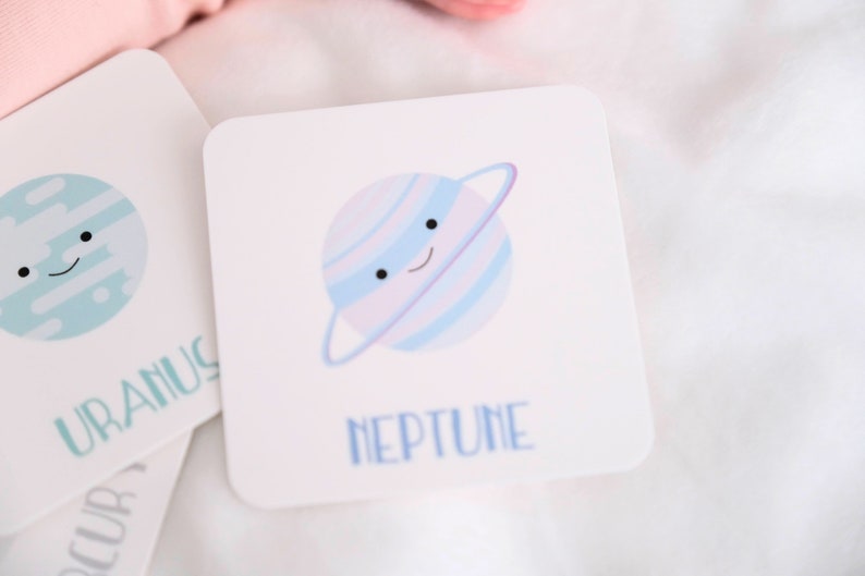 May include: A white card with a blue and purple cartoon planet with a ring around it. The planet has a smiling face. The text "NEPTUNE" is written below the planet.