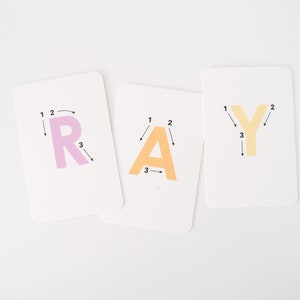 May include: Three white cards with the letters R, A, and Y printed in pink, orange, and yellow. Each letter has numbers 1, 2, and 3 next to it, with arrows indicating the order to trace the letter.