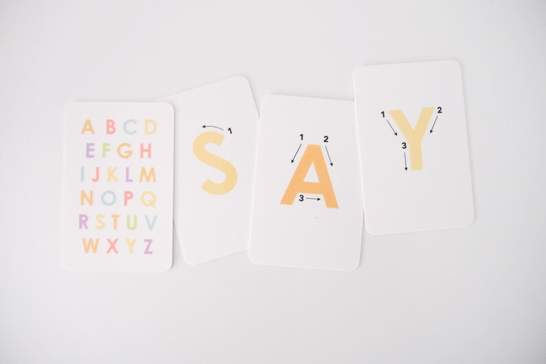 May include: Four white cards with the letters S, A, Y printed in orange. The first card has the alphabet printed in rainbow colors. The other three cards have numbers and arrows showing the order to trace the letters.